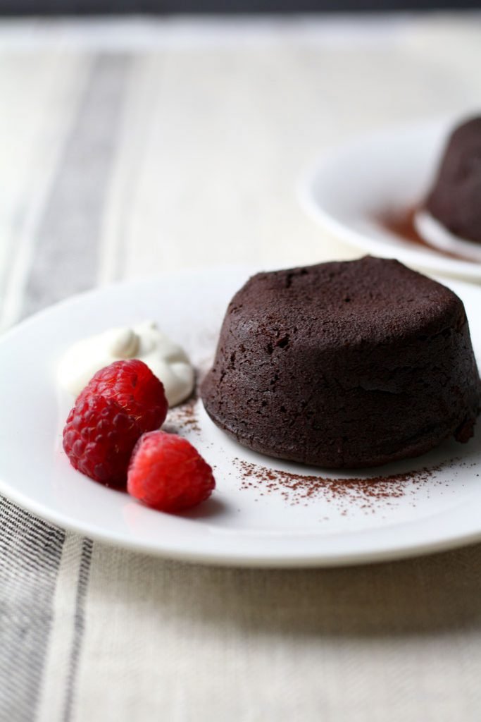 A fresh Chocolate Lava Cake on a plate with creme fraiche and fresh raspberries.