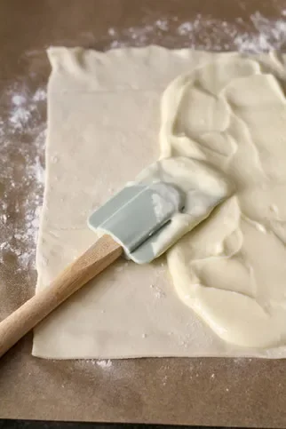 A silicone spatula spreading cream cheese mixture onto puff pastry.