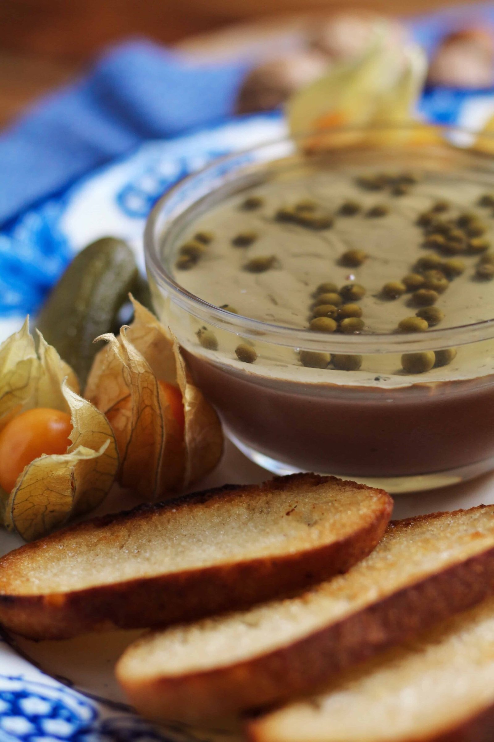 Perfect Chicken Liver Pâté with wine jelly and green peppercorns in a glass bowl with cornichons and baguette