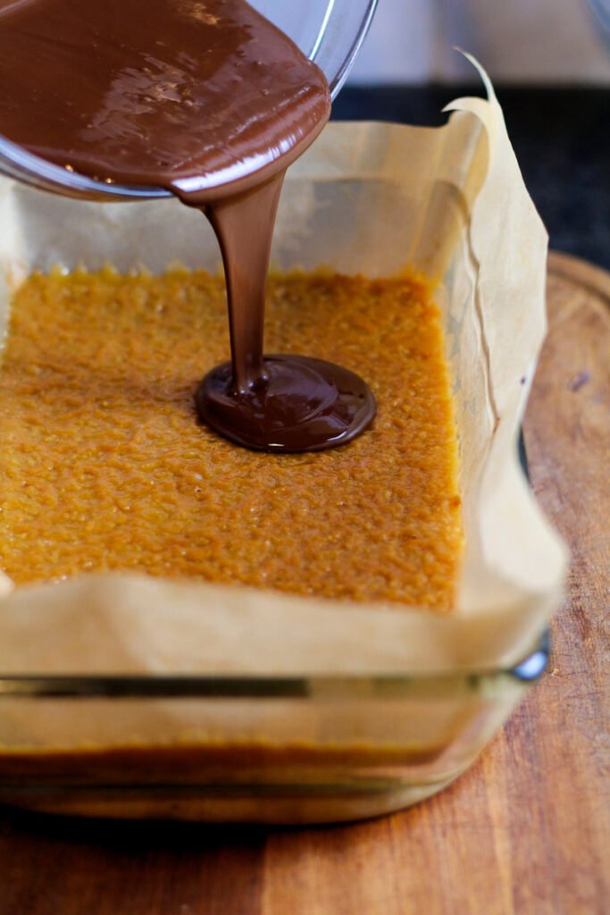 Chocolate pouring onto a layer of caramel.