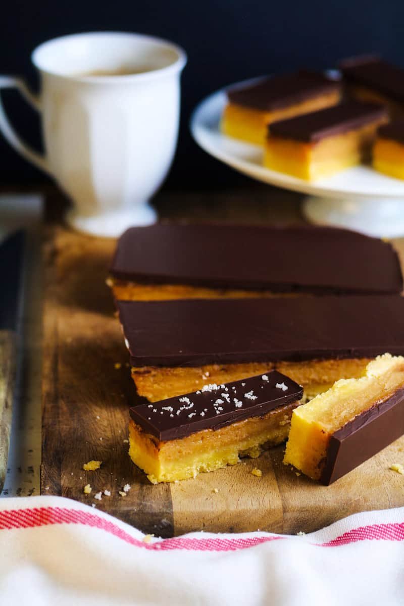 Millionaire's Shortbread sliced on a cutting board with a cup of coffee and a cake stand.