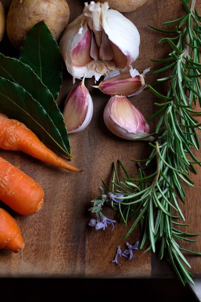 Carrots, Potatoes, Garlic, Rosemary on a chopping board.
