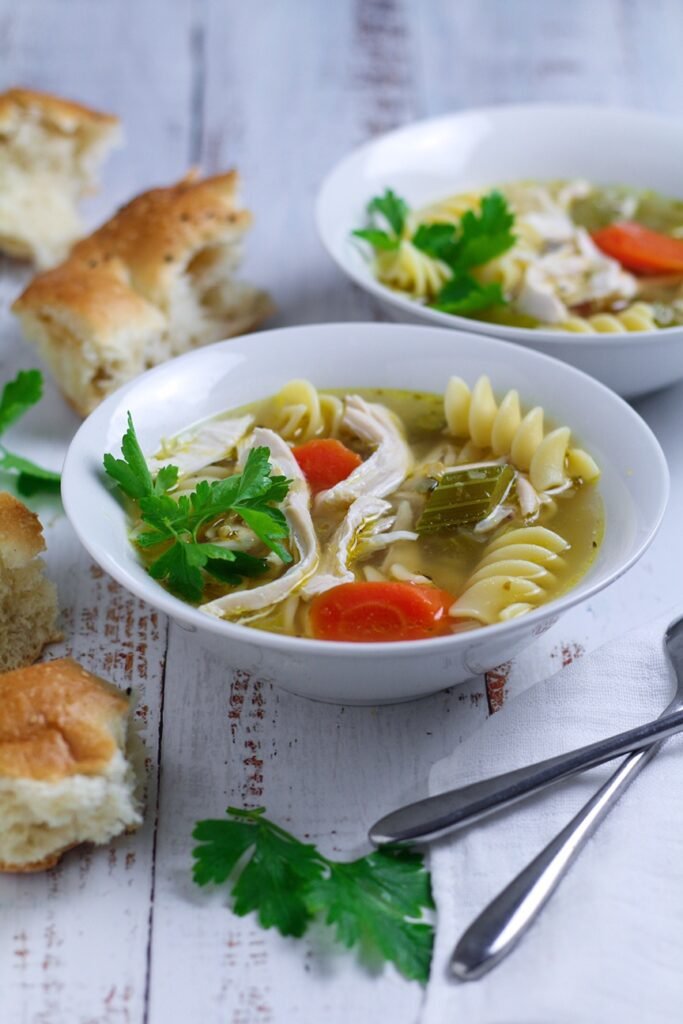 Two bowls of Chicken and Noodle Soup with torn crusty bread.