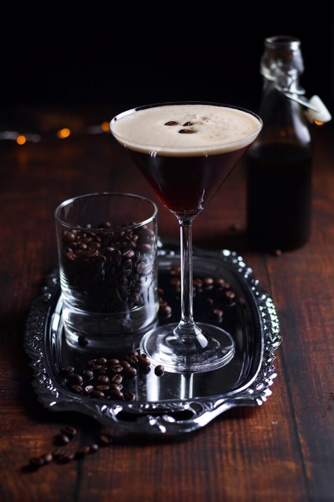 An espresso martini in a martini glass with coffee beans on a silver tray.