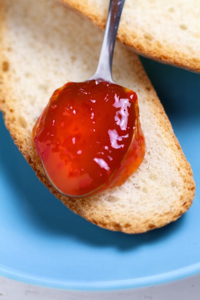 Spicy Red Pepper Jelly on a spoon on top of bread.