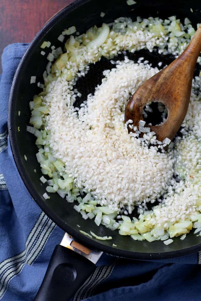 Risotto rice and onion being cooked with butter in a pan.