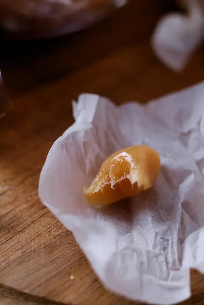 A honey vanilla caramel in a paper wrapper with a boite taken out of it.