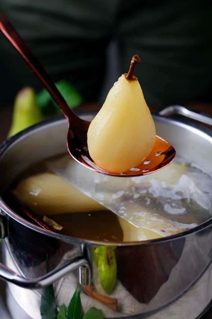 Poached pear being lifted out of a pot.