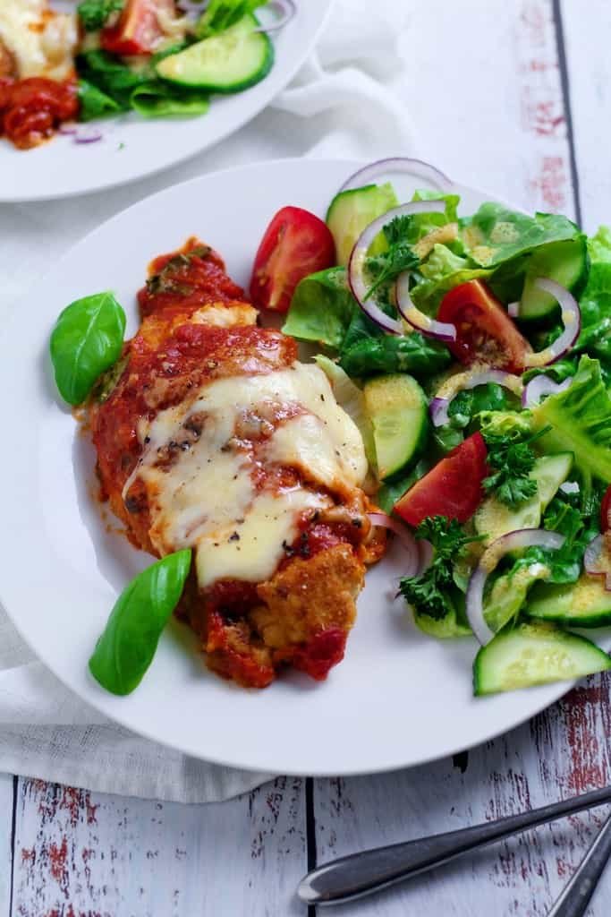 A picture of chicken parmigiana, chicken breast with tomato sauce and melted mozzarella - with salad on a plate