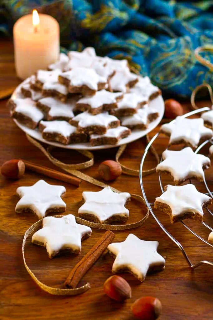 German Cinnamon Star Cookies or Zimtsterne on a wire rack with a candle and Christmas decoration.