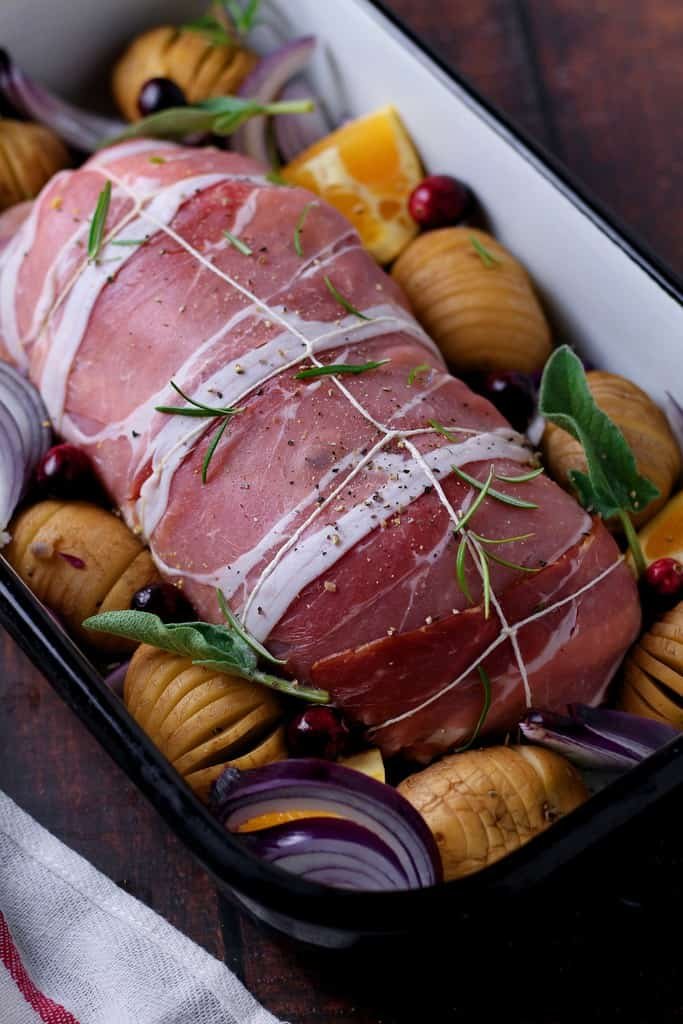 Rolled and unroasted turkey breast in a roasting pan with hasselback potatoes.