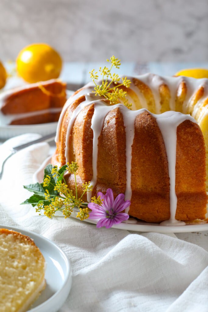 Simple Lemon Bundt Cake on a table with a white cloth, flowers and cut slices.