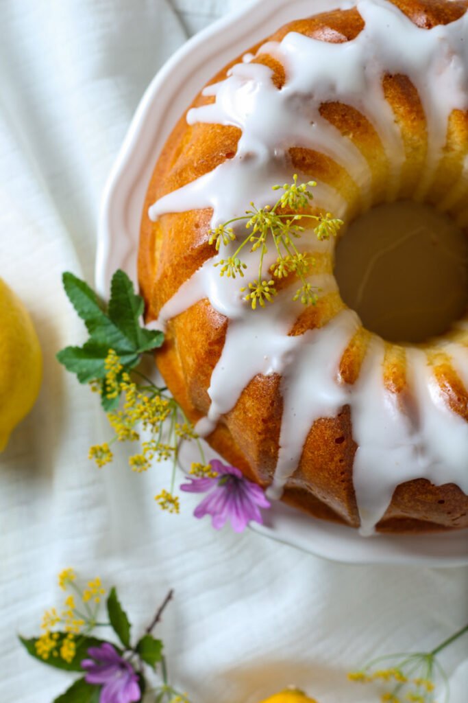 A glazed lemon bundt cake seen from above. Decorated with fresh flowers.