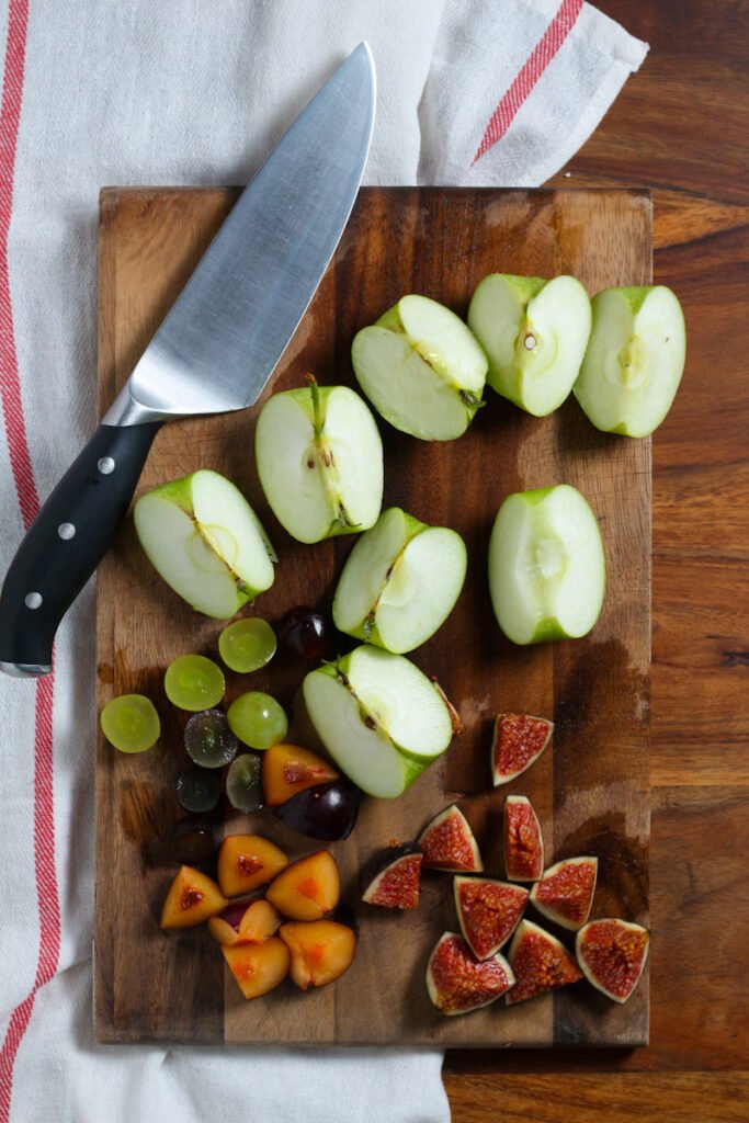 A photo of cut apples, grapes, figs and plums on a chopping board.