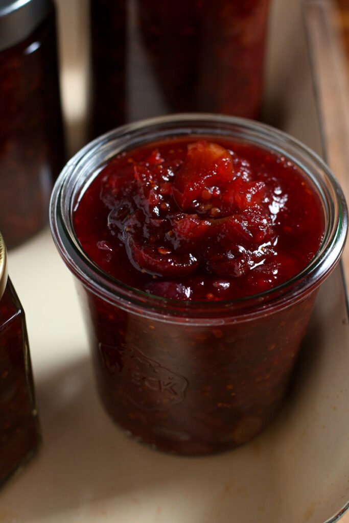 A photo of fruit chutney made with apples, plums, figs and grapes in a glass jar.