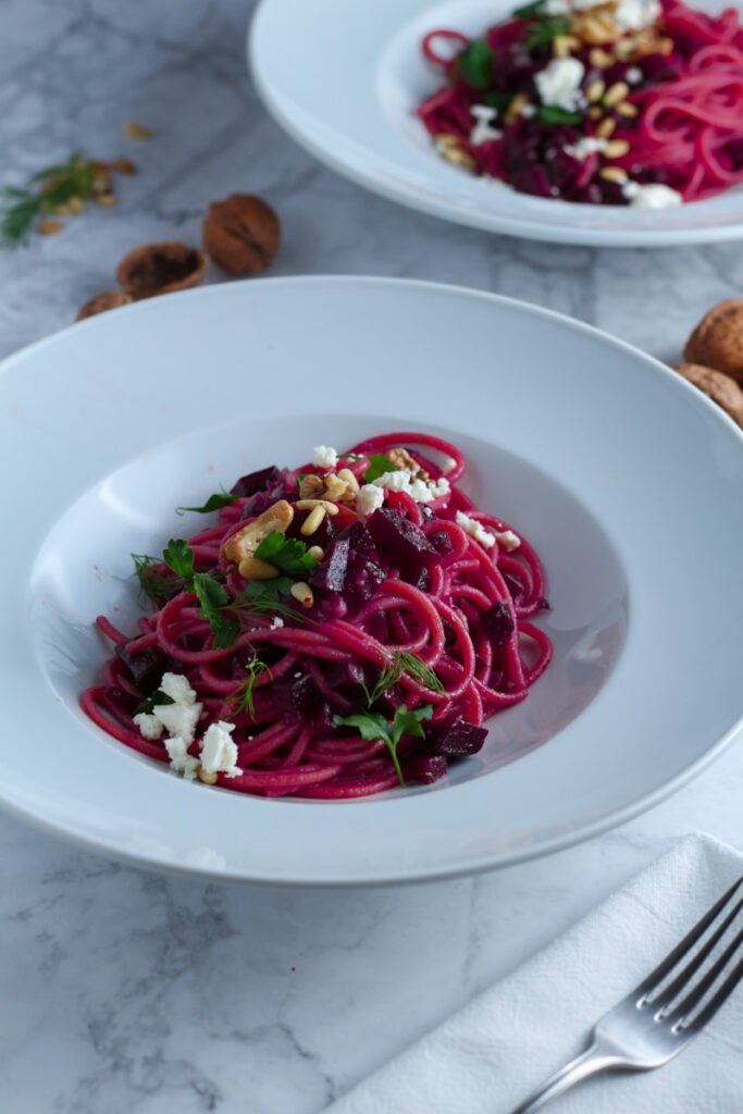 Beetroot and Feta Pasta in a white bowl, topped with toasted nuts and feta cheese