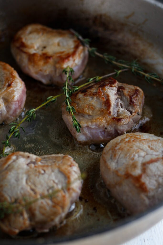 Pork medallions in frying pan with fresh thyme.
