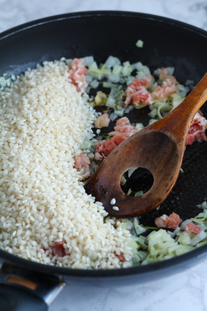 Arborio rice, speck and onion in a pan