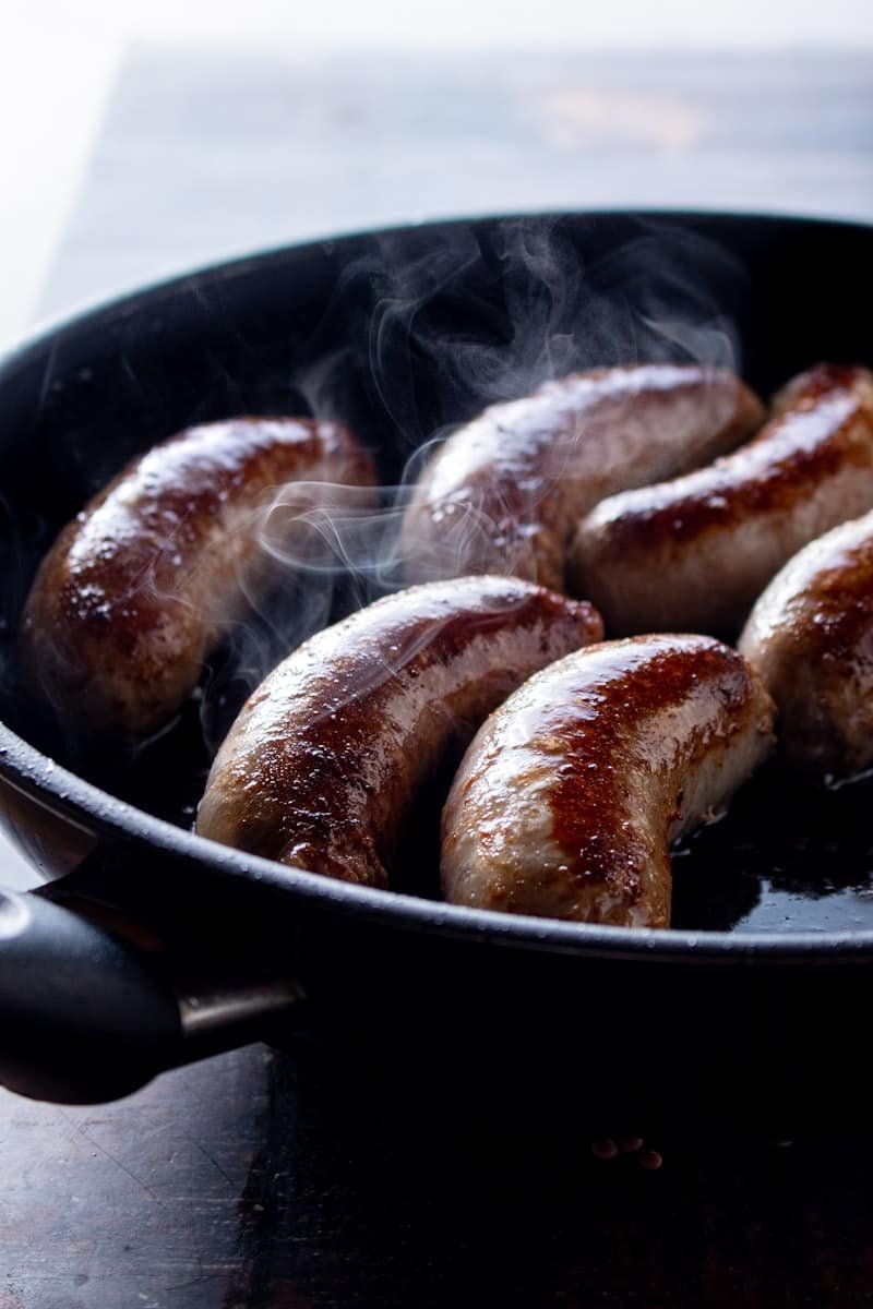 Italian Sausages browning in pan with smoke rising from the sausages.
