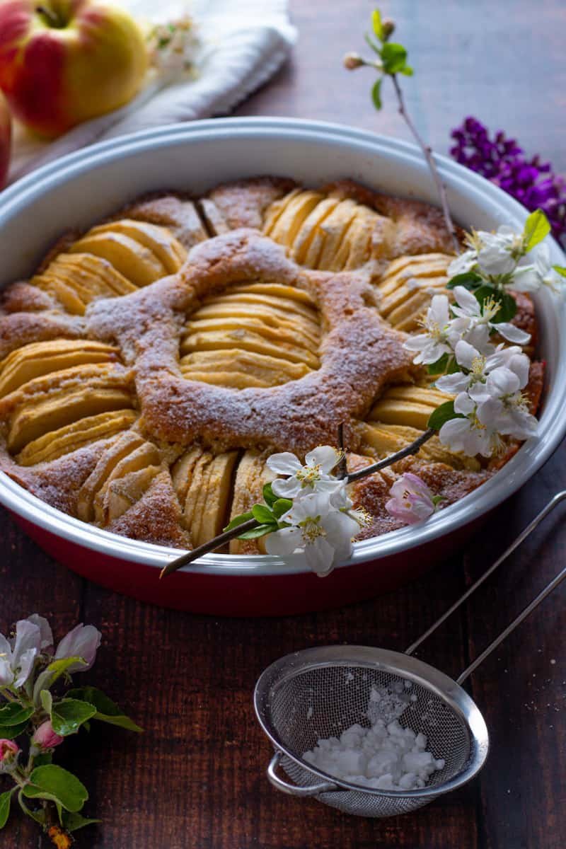 Easy German Apple Cake baked in a pie dish with fresh apple blossoms on top.