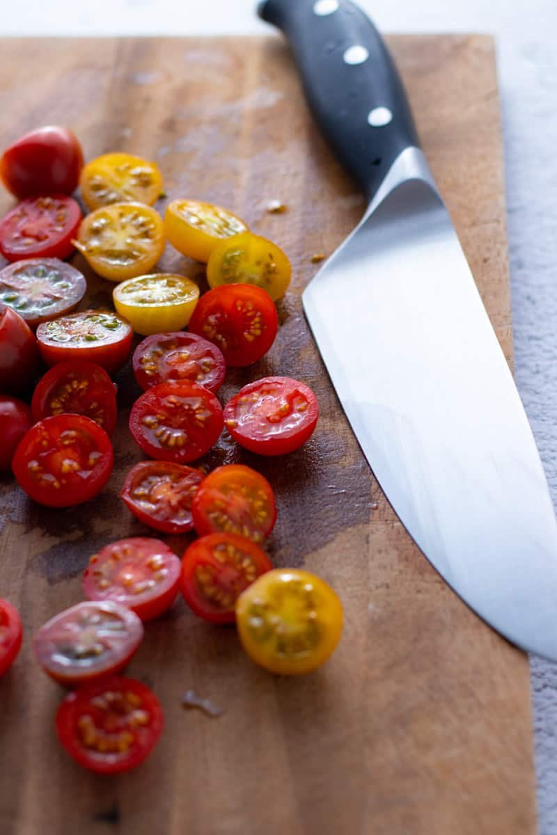 Halved cherry tomatoes on a wooden chopping board with a chef's knife