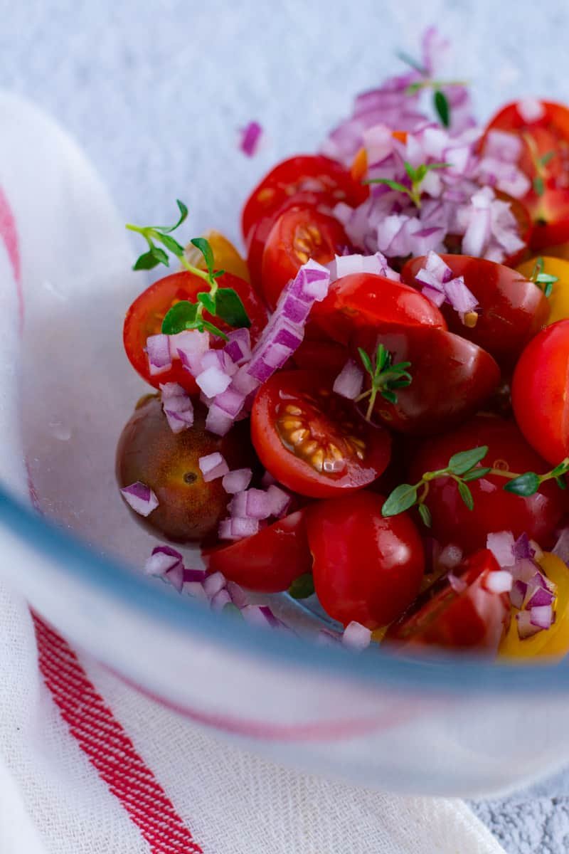 Diced red onion, cherry tomatoes and herbs in a bowl