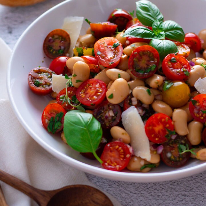 Cherry Tomato and White Bean Salad in a bowl with wooden salad servers and a baguette