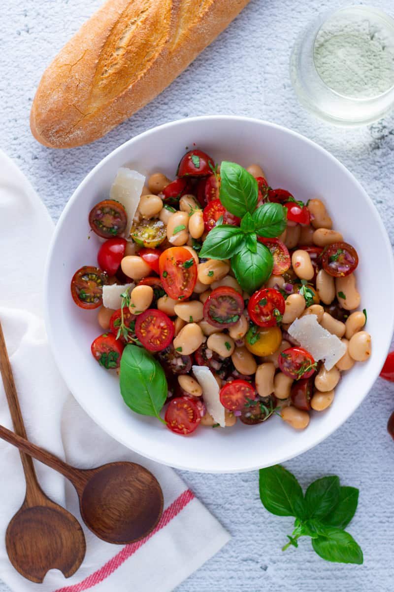 Cherry Tomato and White Bean Salad in a bowl with wooden salad servers and a baguette