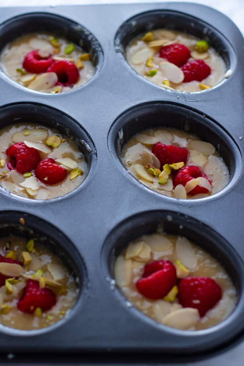 Friand batter topped with raspberries, almonds and pistachios in a friand pan