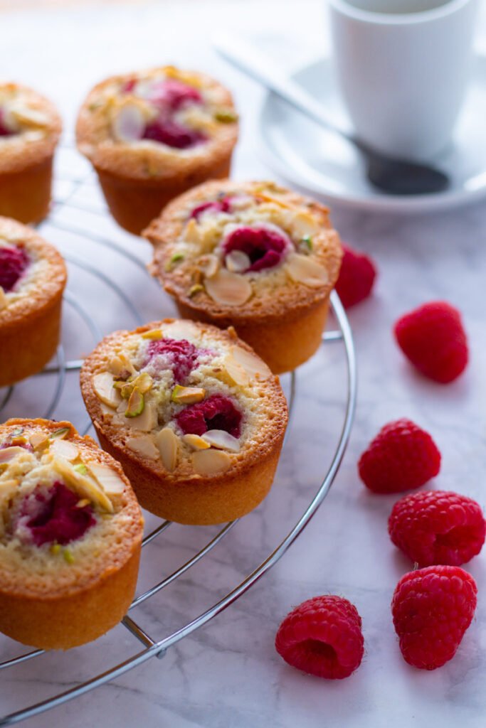 Raspberry and Almond Friands on a cooling rack with fresh raspberries and a cup of espresso