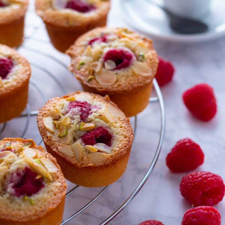 Raspberry and Almond Friands on a cooling rack with fresh raspberries and a cup of espresso