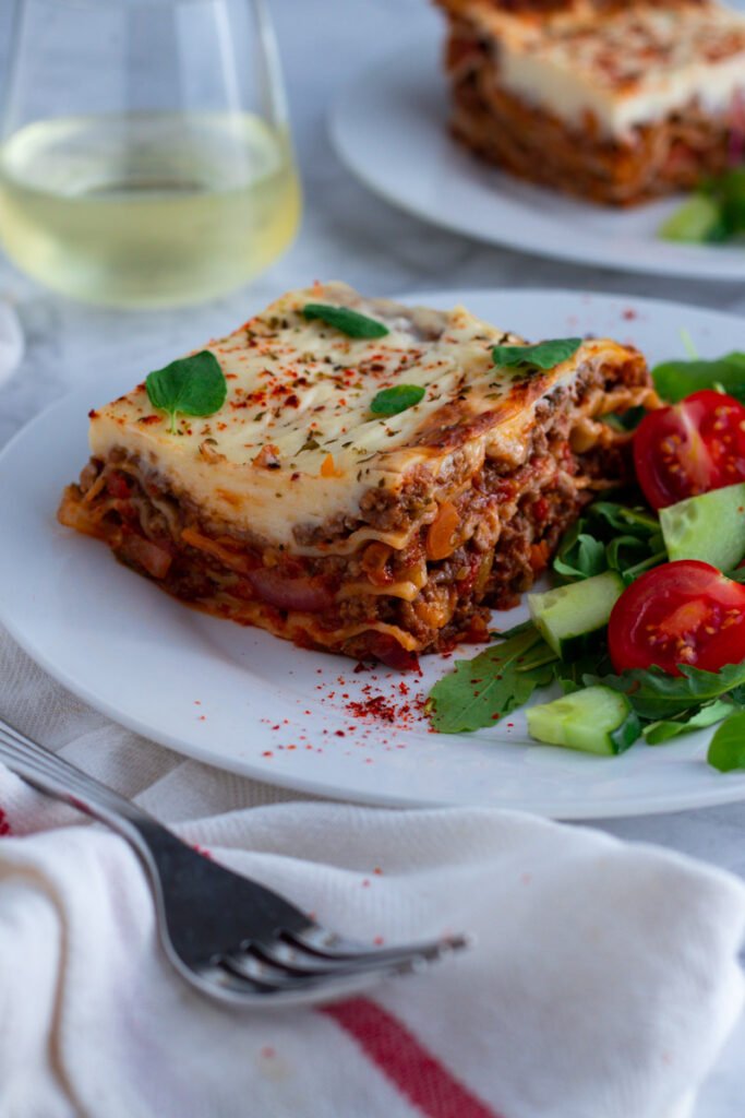 A picture of a classic Italian Lasagne al forno served with fresh green salad and a glass of white wine