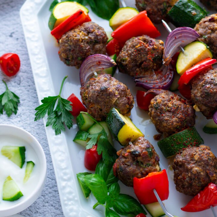 Mediterranean meatball skewers with mixed vegetables on a white plate