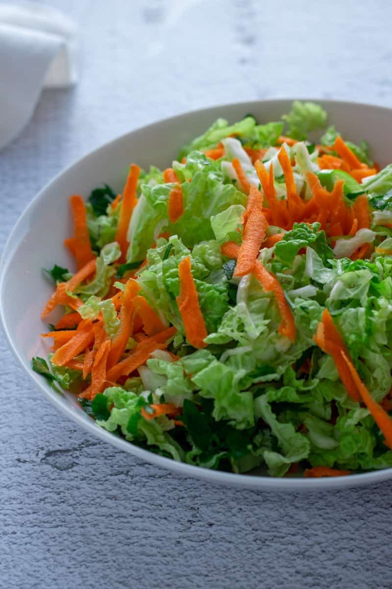 Sliced Chinese cabbage, carrot, parsley and spring onion coleslaw in a bowl