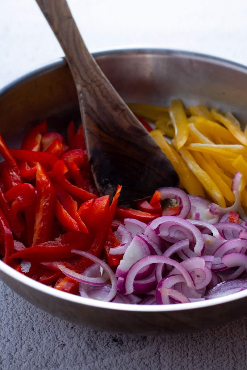 Scliced red onion, red pepper and yellow pepper in a frying pan