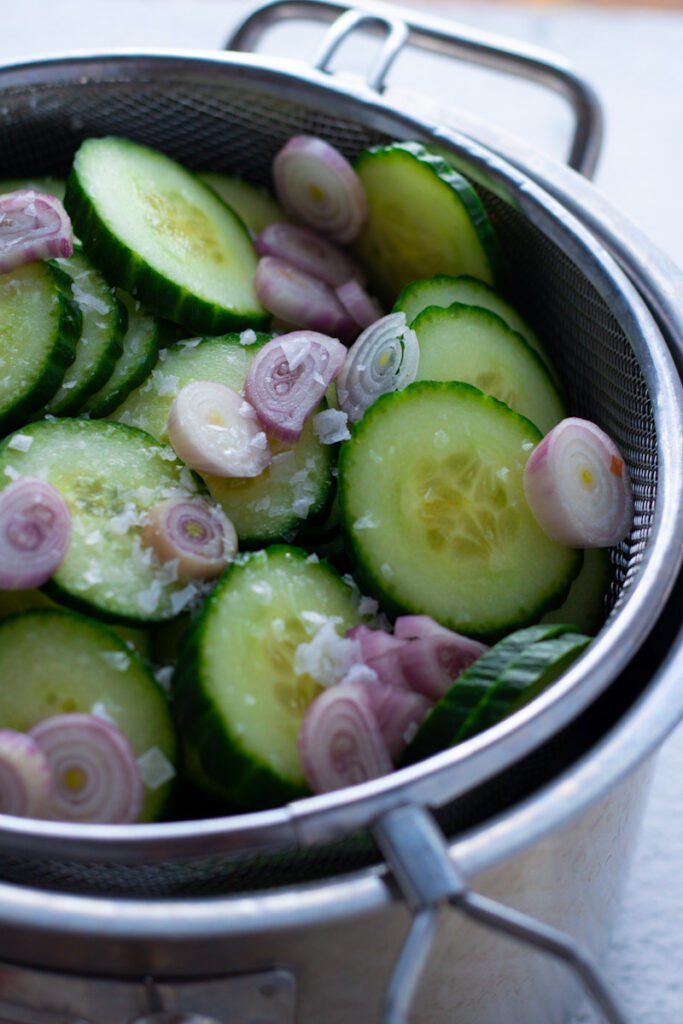 Sliced cucumbers and shallots draining in a sieve