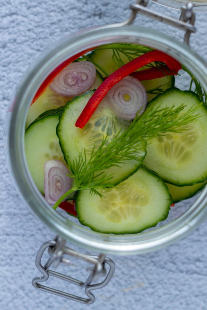 Cucumber, pepper, dill and shallots packed into a glass jar