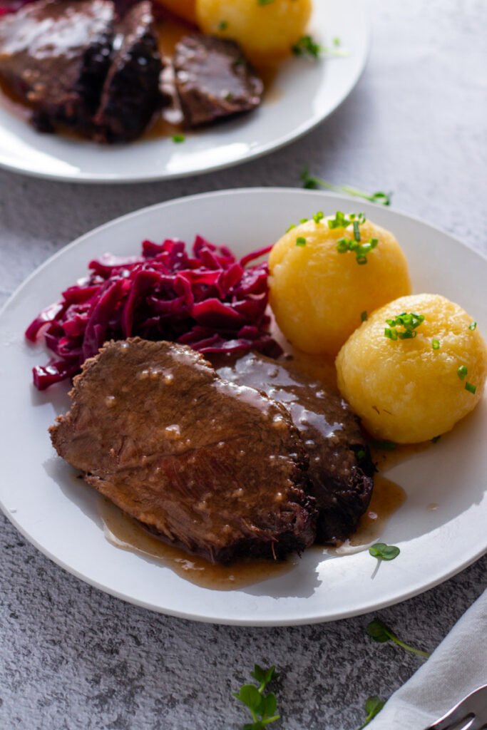 German Sauerbraten beef roast on a plate with red cabbage and potato dumplings.