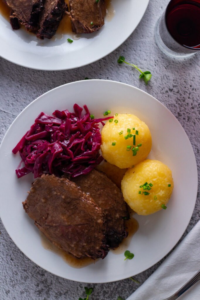 Sauerbraten on a plate with potato dumplings and red cabbage.