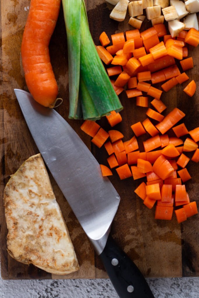 Celery, leek and carrots for Sauerbraten sauce on a cutting board with a chef's knife.