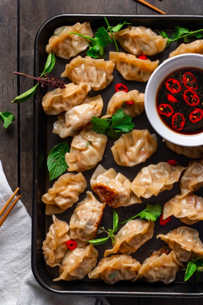Pork and Shrimp Gyoza on a tray with spicy dipping sauce and fresh herbs.