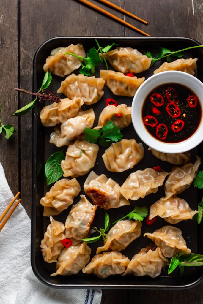 Pork and Shrimp Gyoza on a tray with spicy dipping sauce and fresh herbs.