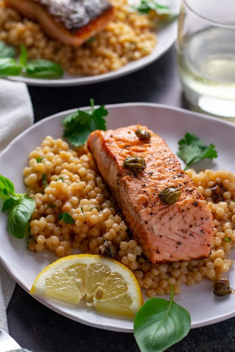 Lemon and Caper Salmon with herby couscous on a serving plate with a glass of white wine.