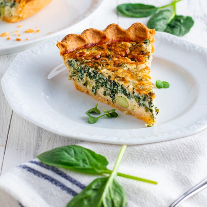 A slice of coronation quiche on a plate with fresh spinach.