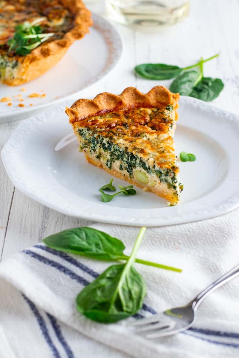 A slice of coronation quiche on a plate with fresh spinach.
