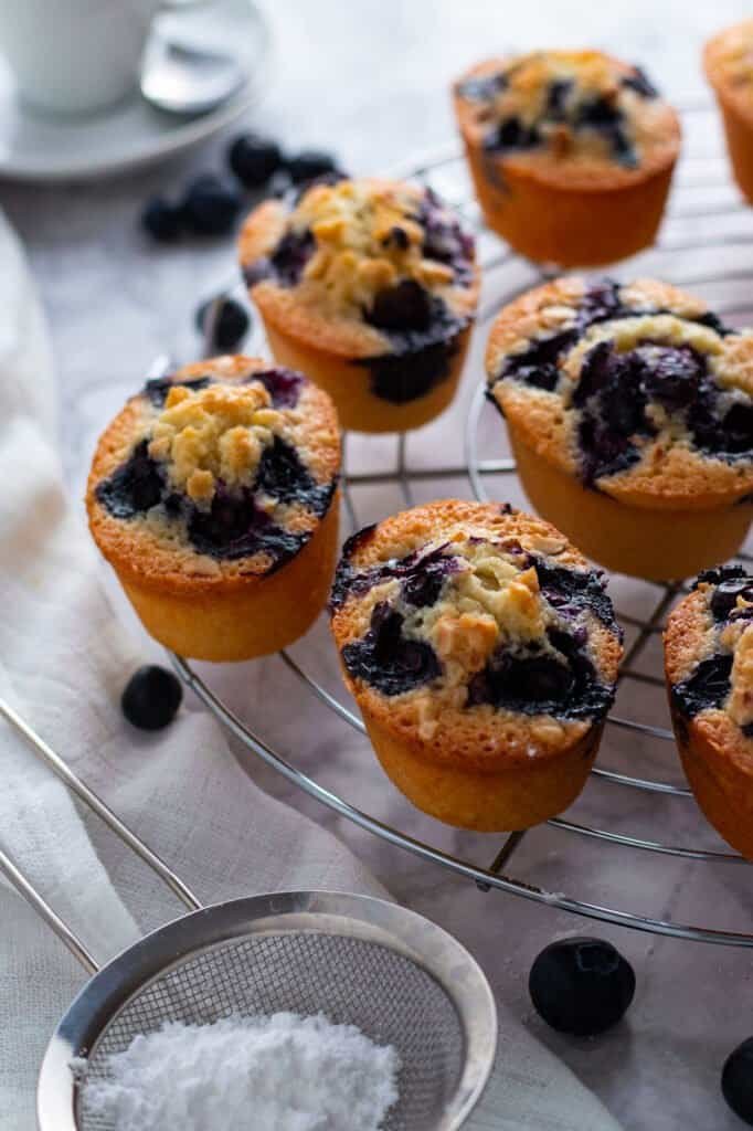 Blueberry friands on a cooling rack with icing sugar and an espresso.