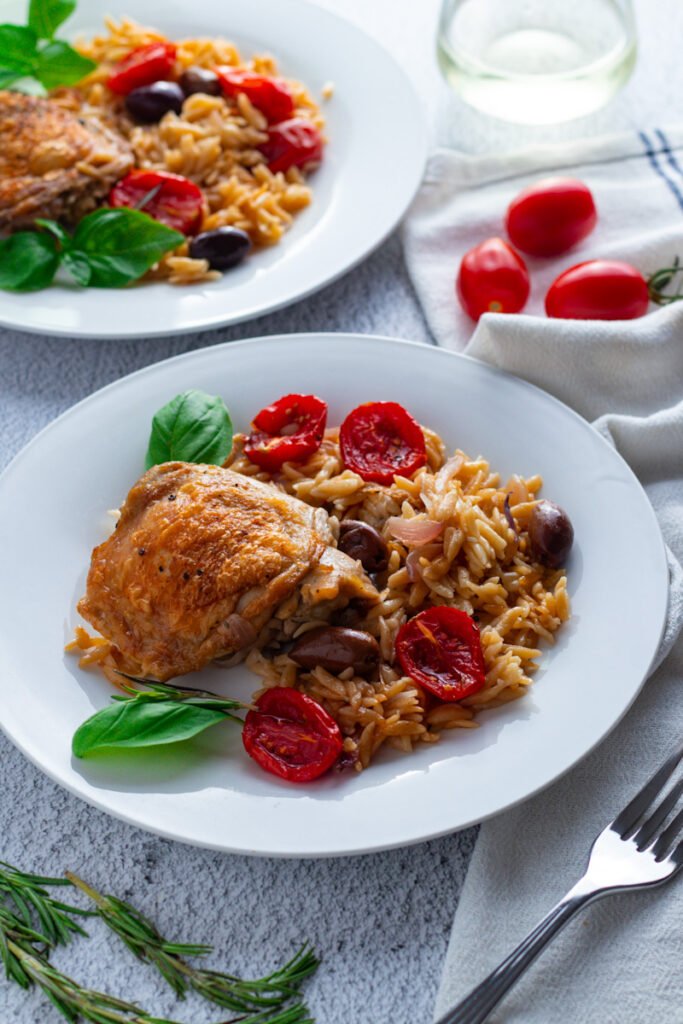 One pan chicken and orzo on a plate with white wine and fresh herbs.