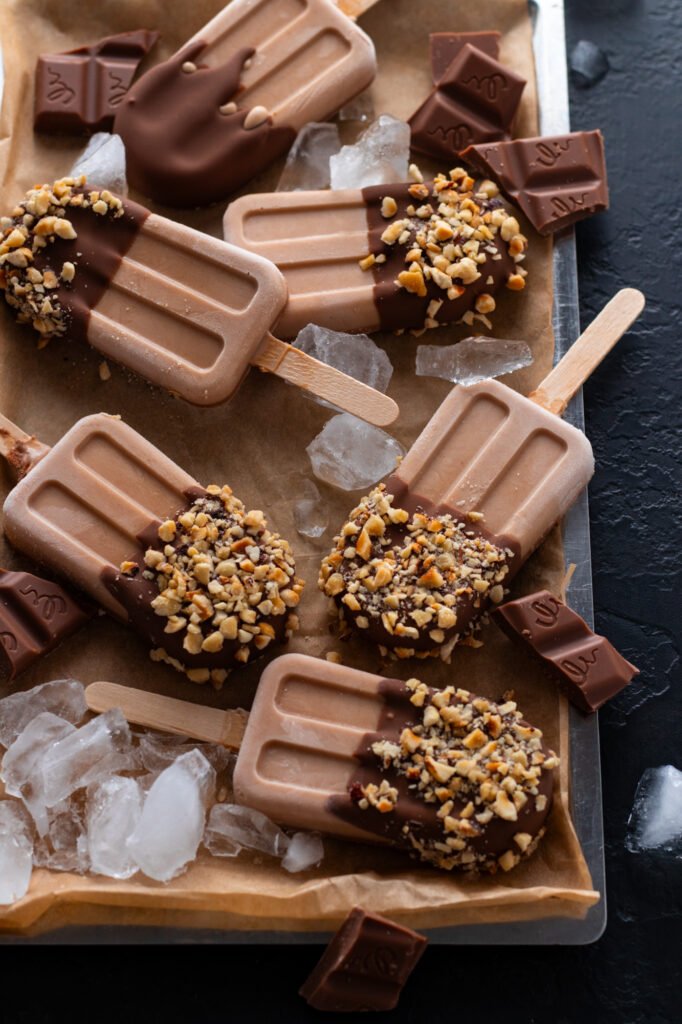 Homemade Chocolate popsicles dipped in chocolate and nuts on a tray.