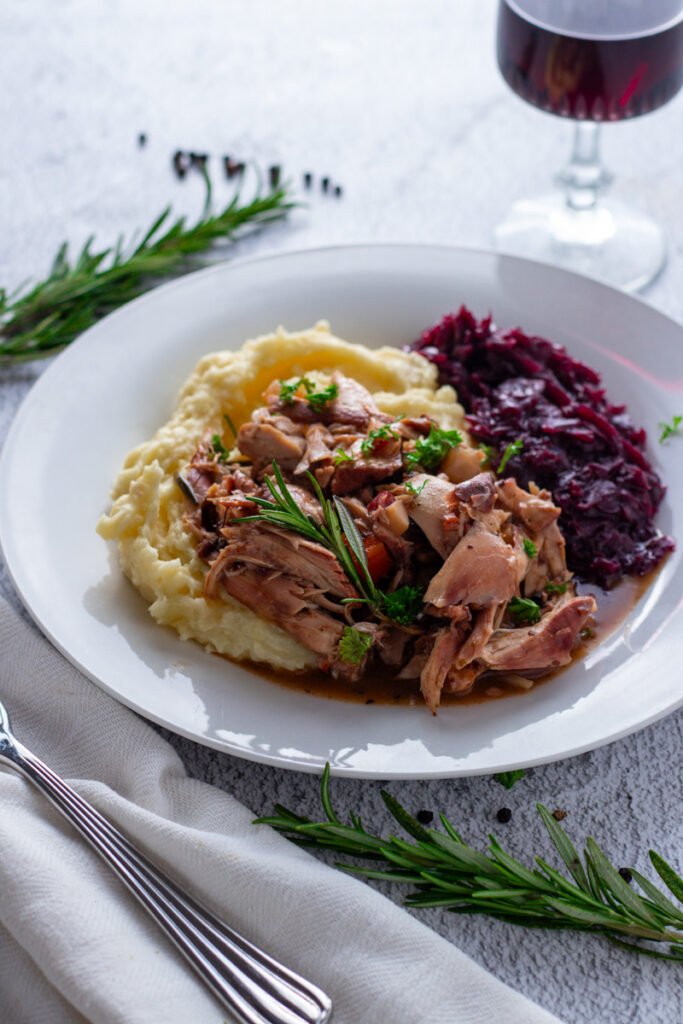 A plate of Hasenpfeffer German Rabbit Stew with braised red cabbage and mashed potatoes.