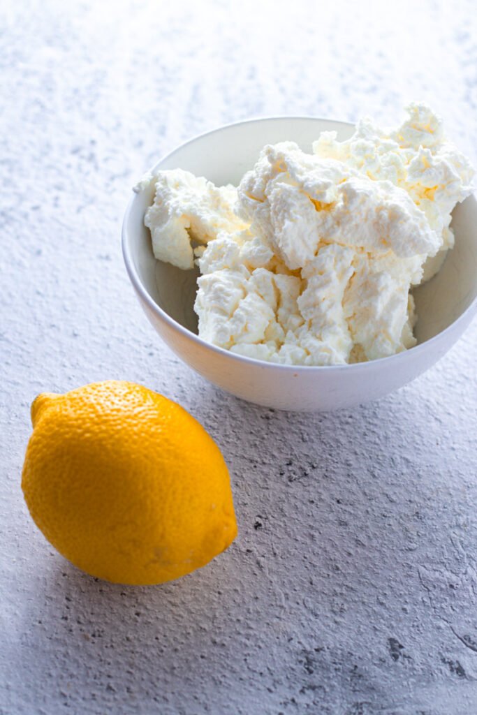 Fresh ricotta in a bowl and a lemon.